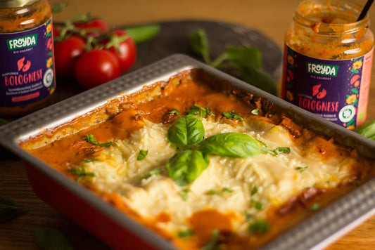 Vegane Lasagne Bolognese mit Froyda Sunflower Bolognese. Lasagne in Backform, daneben zwei leere Gläser Froyda Sunflower Bolognese, Tomaten und Basilikum.