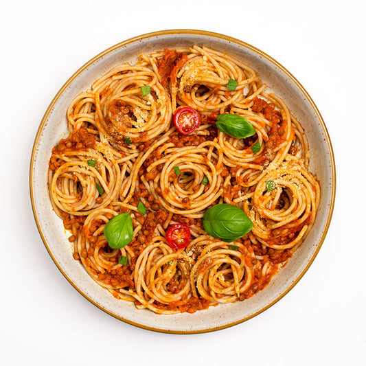 Bowl of Froyda Lentil Bolognese with rice spaghetti and basil leaves on white background.